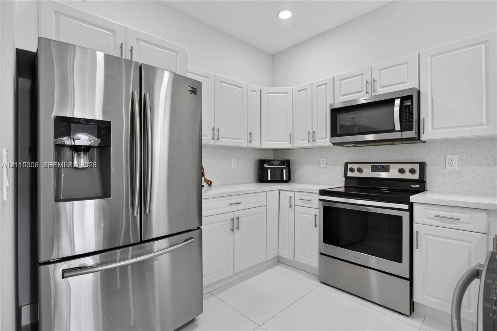 4812 NW 19th Street, Coconut Creek, FL 33063 Kitchen featuring white shaker-style cabinetry, stainless steel refrigerator, over-the-range microwave, electric range, and light-toned solid surface countertops
