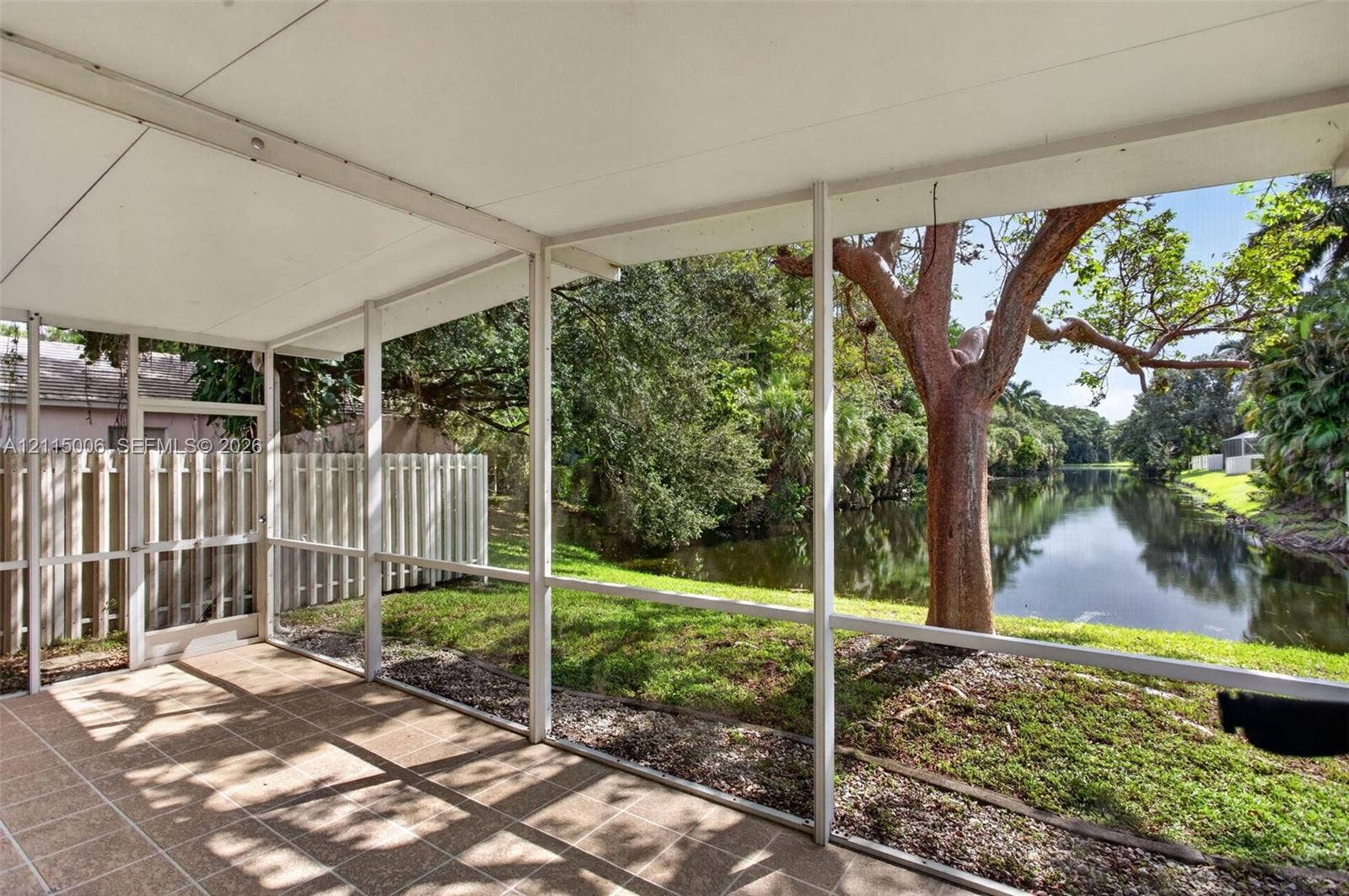4812 NW 19th Street, Coconut Creek, FL 33063 Screened-in patio with tile flooring and white structural frame overlooking a water feature and mature landscaping
