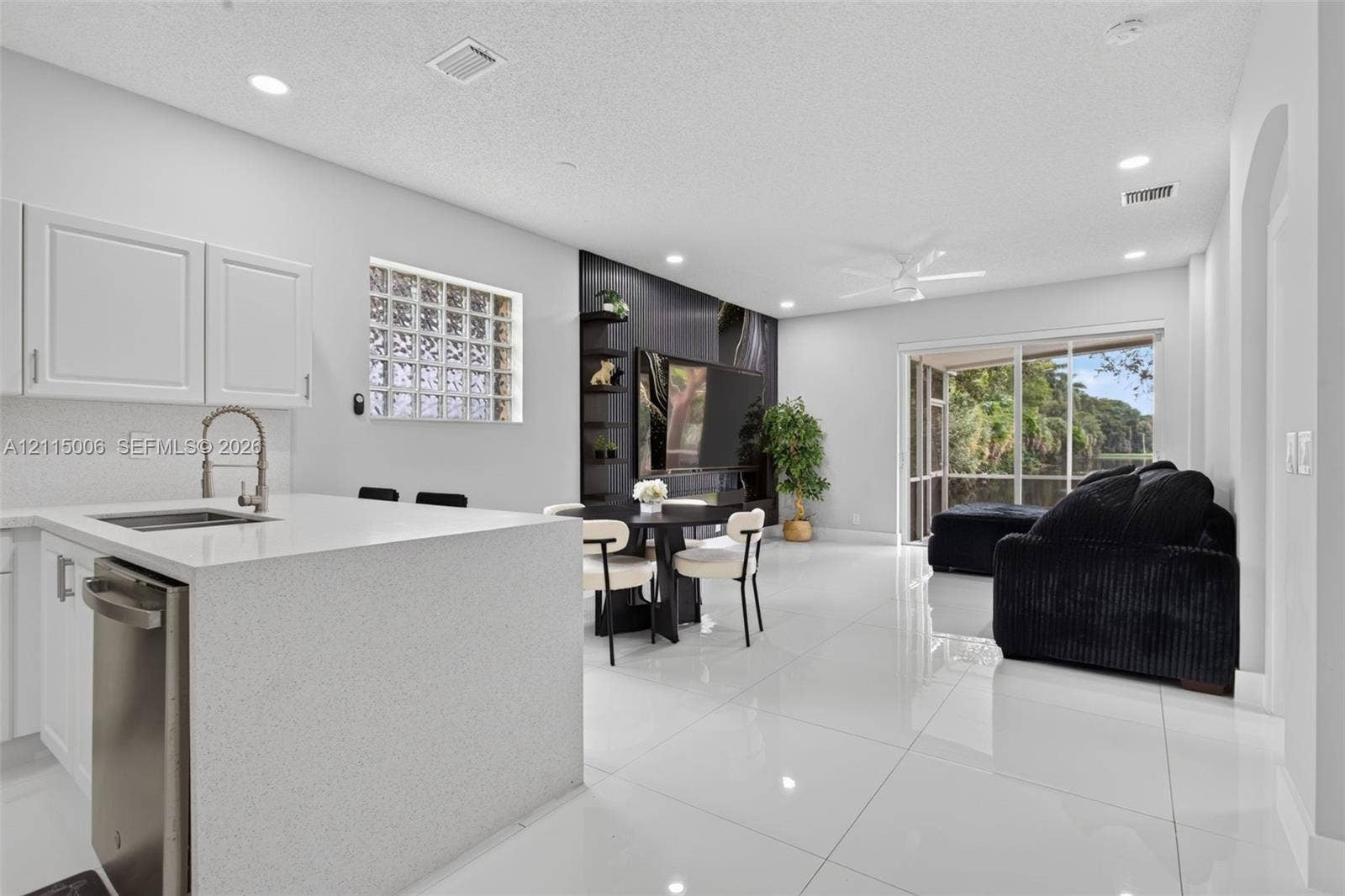 4812 NW 19th Street, Coconut Creek, FL 33063 Kitchen featuring a waterfall-edge quartz island, stainless steel dishwasher, glass block accent window, and high-gloss floor tile