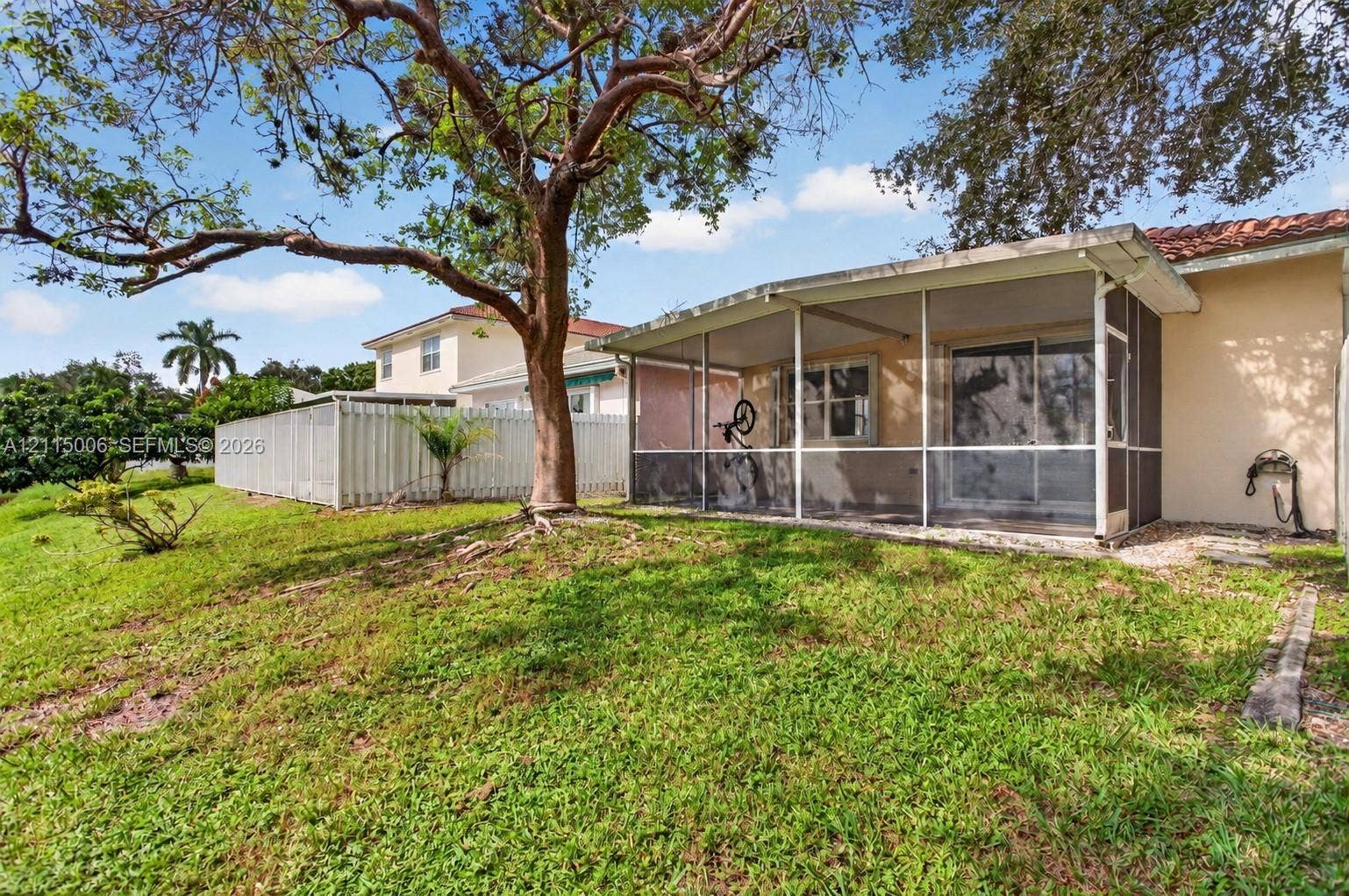 4812 NW 19th Street, Coconut Creek, FL 33063 Screened-in porch featuring a metal frame and tile-surfaced patio area, complemented by a grass-covered backyard and mature shade trees