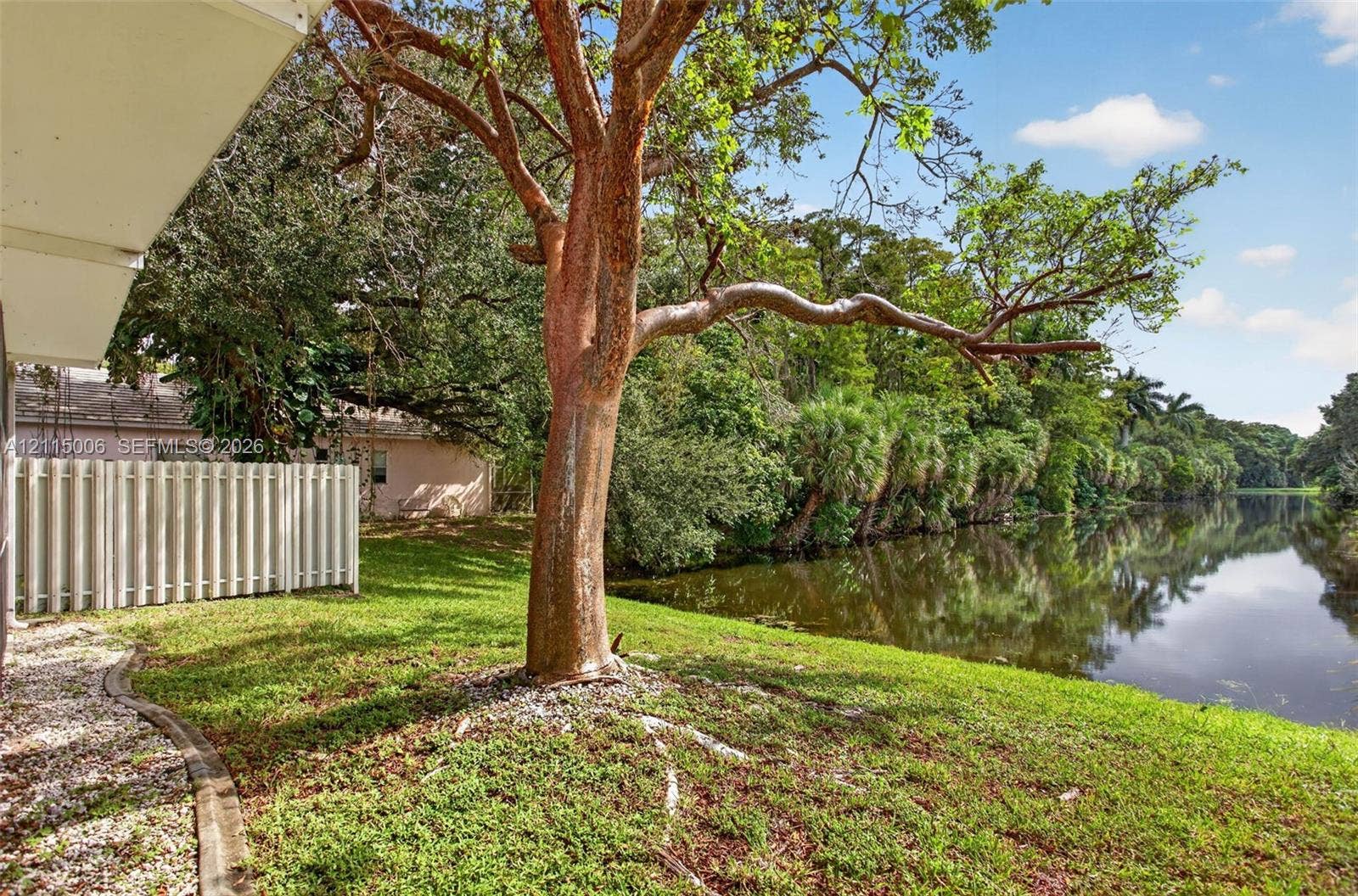 4812 NW 19th Street, Coconut Creek, FL 33063 Waterfront backyard featuring a grass lawn, mature trees, and a privacy fence