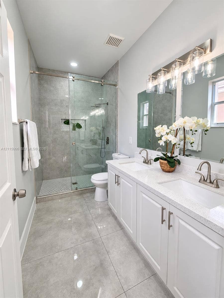4812 NW 19th Street, Coconut Creek, FL 33063 Double vanity featuring white shaker-style cabinetry, quartz countertops, and dual undermount sinks, complemented by a walk-in shower with a glass enclosure, floor-to-ceiling tile surround, and polished nickel fixtures