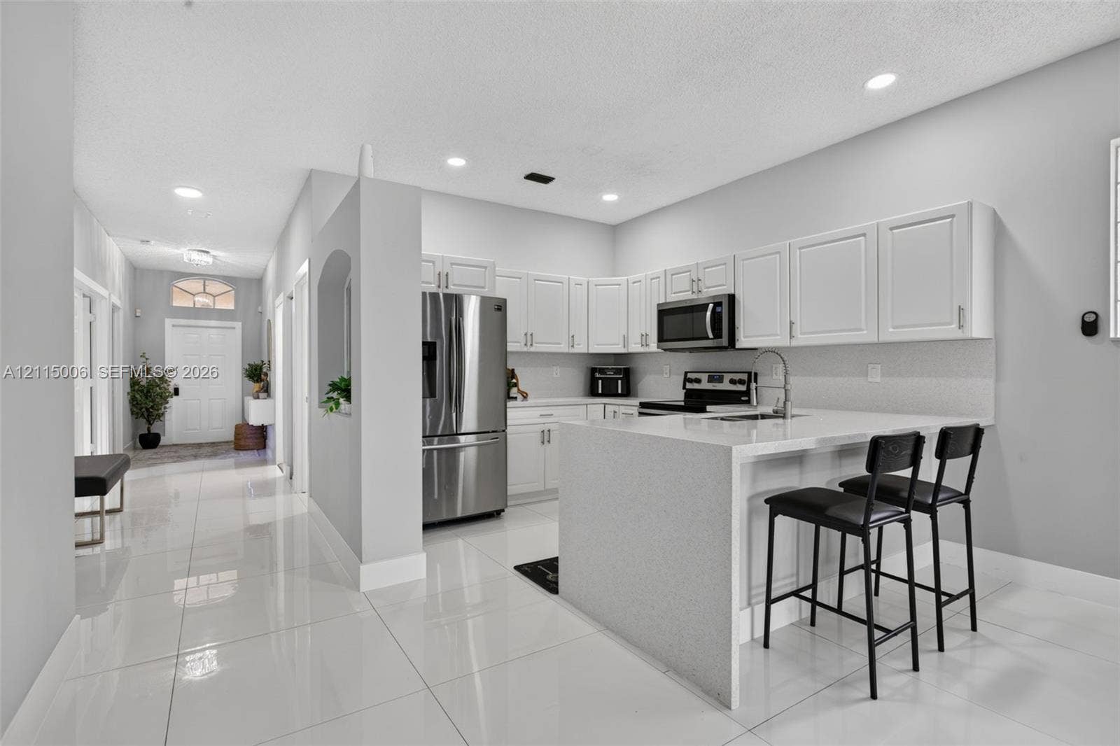 4812 NW 19th Street, Coconut Creek, FL 33063 Kitchen featuring white cabinetry, solid surface countertops, stainless steel appliances, a peninsula with seating space, and polished tile flooring