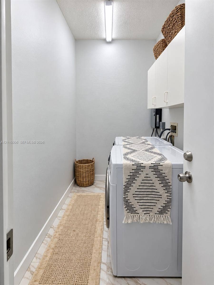 4812 NW 19th Street, Coconut Creek, FL 33063 Utility space featuring stone-look tile flooring, white shaker-style wall-mounted cabinetry, and a linear overhead light fixture