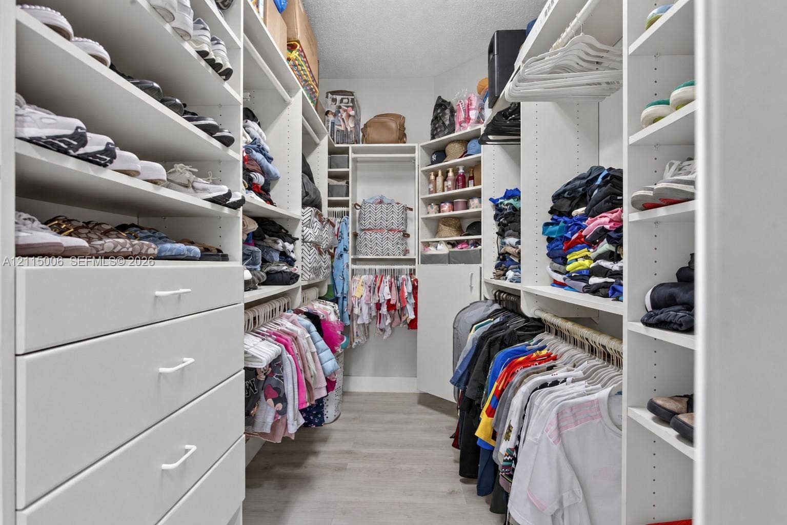 4812 NW 19th Street, Coconut Creek, FL 33063 Custom walk-in closet featuring white built-in shelving, multiple hanging rods, integrated storage drawers with bar pulls, and wood-finish flooring