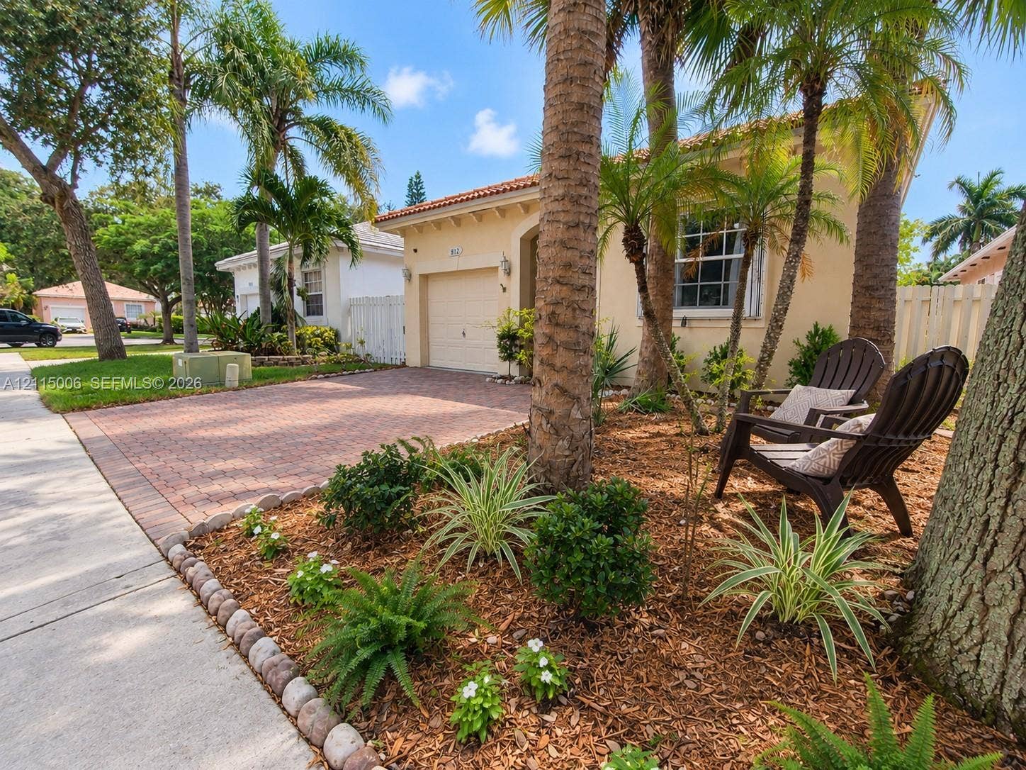 4812 NW 19th Street, Coconut Creek, FL 33063 Stucco exterior featuring a tile roof, brick-paver driveway, single-car garage, and mulched landscaping with mature palm trees