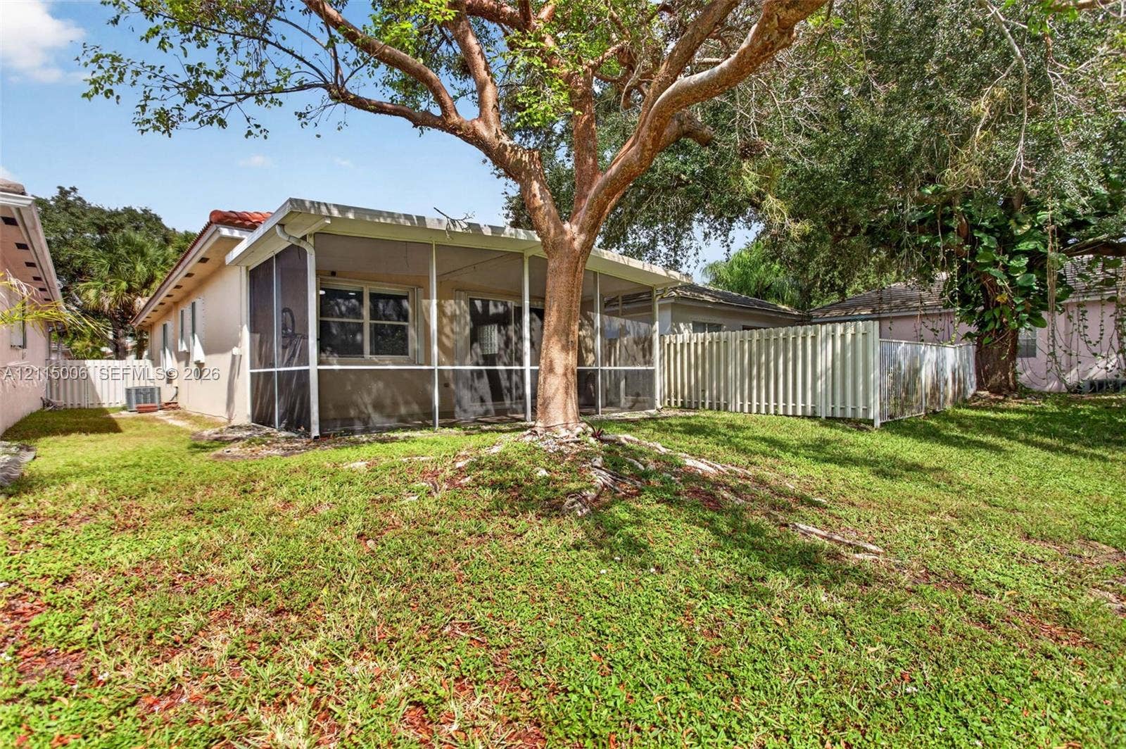 4812 NW 19th Street, Coconut Creek, FL 33063 Screened-in rear porch featuring a red tile roof, mature landscaping, and white privacy fencing