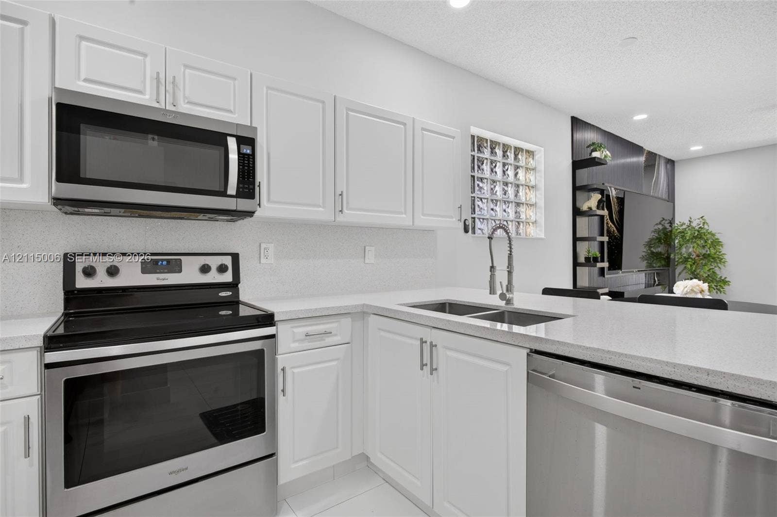 4812 NW 19th Street, Coconut Creek, FL 33063 Kitchen featuring white shaker-style cabinetry, stainless steel appliances, light-toned solid surface countertops, a dual-basin stainless steel undermount sink with a gooseneck faucet, and a glass block window