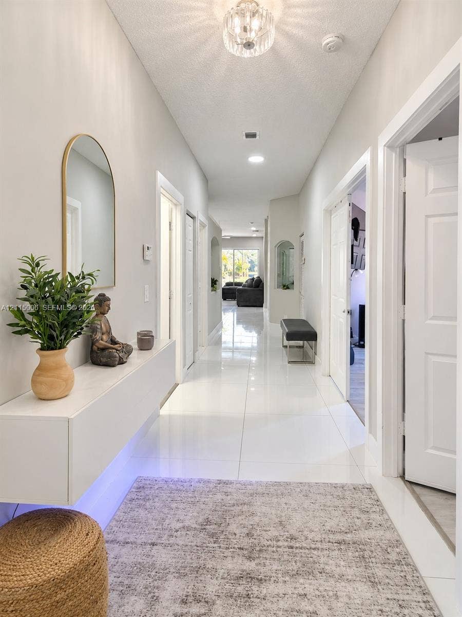 4812 NW 19th Street, Coconut Creek, FL 33063 Hallway featuring large-format tile flooring, a wall-mounted floating console, an arched wall mirror, and a decorative flush-mount ceiling fixture