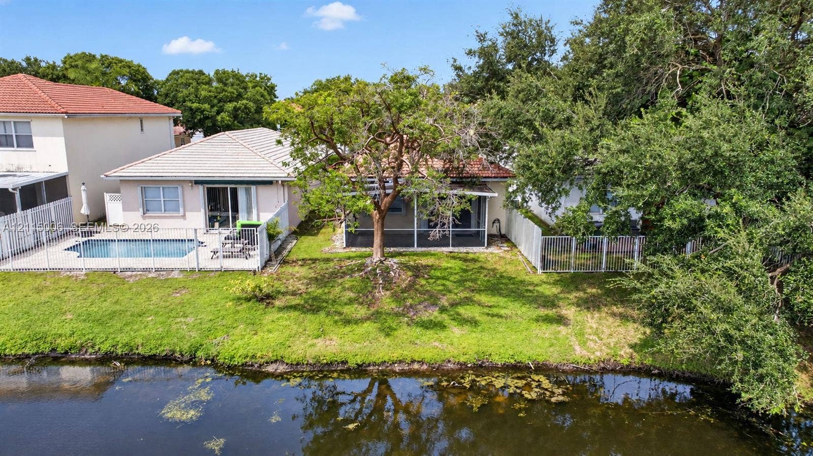 4812 NW 19th Street, Coconut Creek, FL 33063 Waterfront exterior featuring a screen-enclosed patio, in-ground pool with concrete surround, perimeter white metal fencing, and mature landscaping