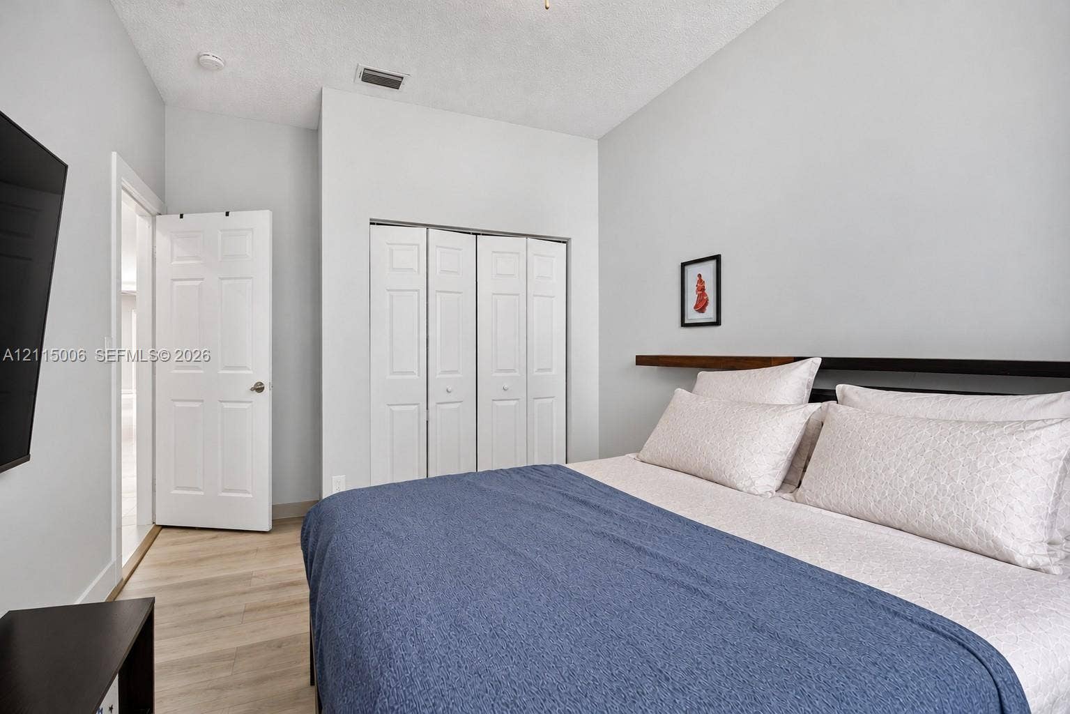 4812 NW 19th Street, Coconut Creek, FL 33063 Bedroom featuring wood-finish flooring, a built-in closet with four-panel folding doors, and a wall-mounted wood floating shelf