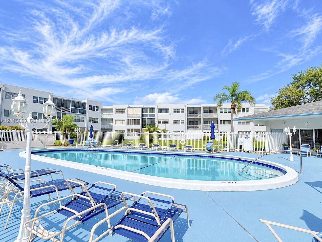 2300 Park Lane, #105, Hollywood, FL 33021 Oval swimming pool with a concrete deck, metal perimeter fencing, and decorative exterior lamp posts