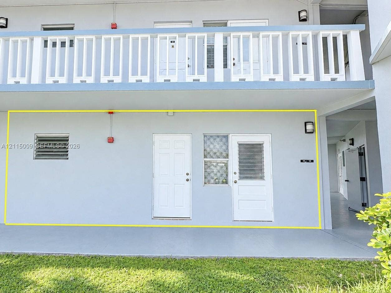 2300 Park Lane, #105, Hollywood, FL 33021 Exterior facade featuring a ground-level concrete patio, a louvered wall vent, solid-core panel doors, and a decorative glass block window accent