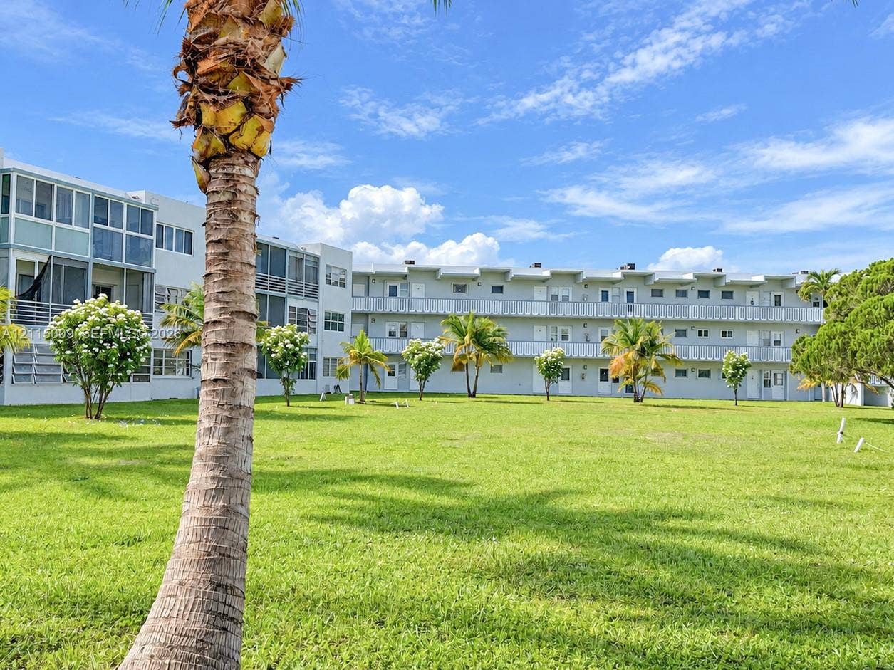 2300 Park Lane, #105, Hollywood, FL 33021 Multi-level exterior featuring light-colored facade, screened balcony enclosures, exterior metal railings, and expansive common grass area with mature palm trees