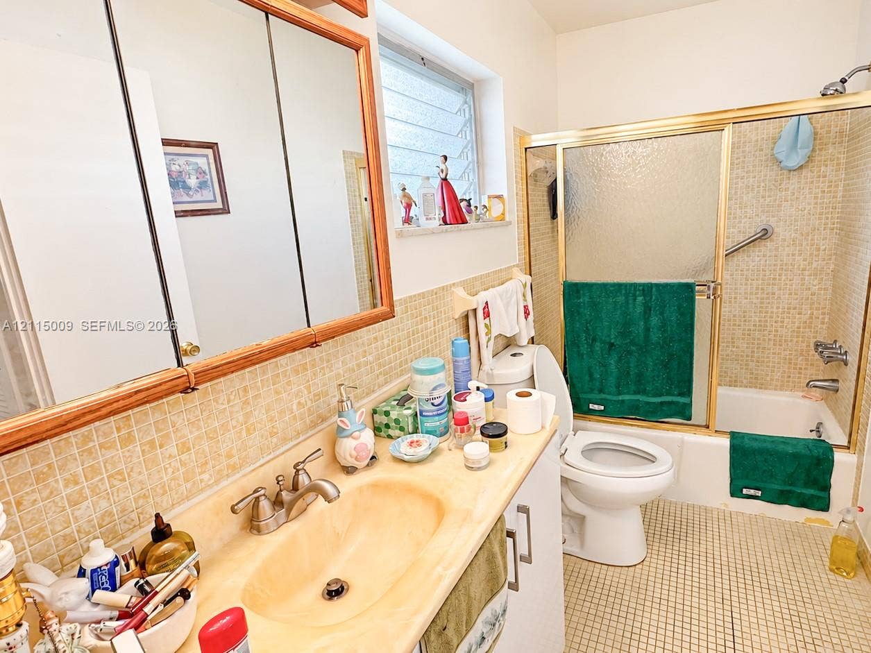 2300 Park Lane, #105, Hollywood, FL 33021 Bathroom featuring a single-basin vanity with an integrated countertop, tri-fold medicine cabinet, louvered window, and a shower-tub combination with sliding glass doors