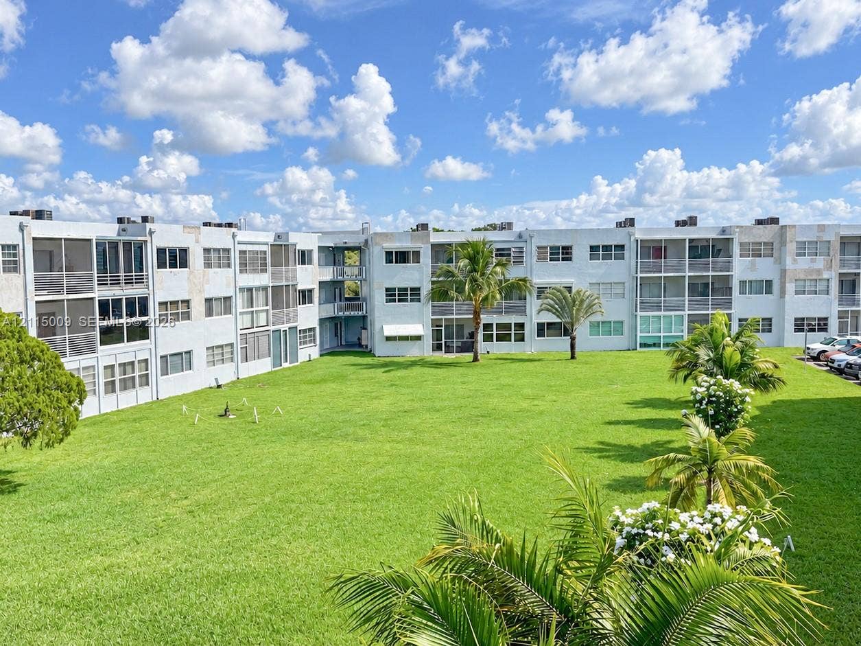 2300 Park Lane, #105, Hollywood, FL 33021 Multi-story residential building featuring screened balconies, expansive communal lawn, mature palm trees, and structural stucco exterior