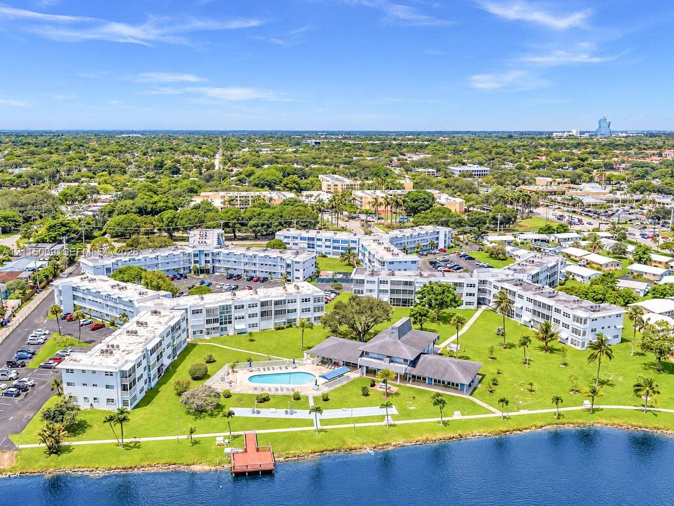 2300 Park Lane, #105, Hollywood, FL 33021 Aerial perspective of a multi-building residential complex featuring a community swimming pool, waterfront dock, expansive green space, and paved surface parking