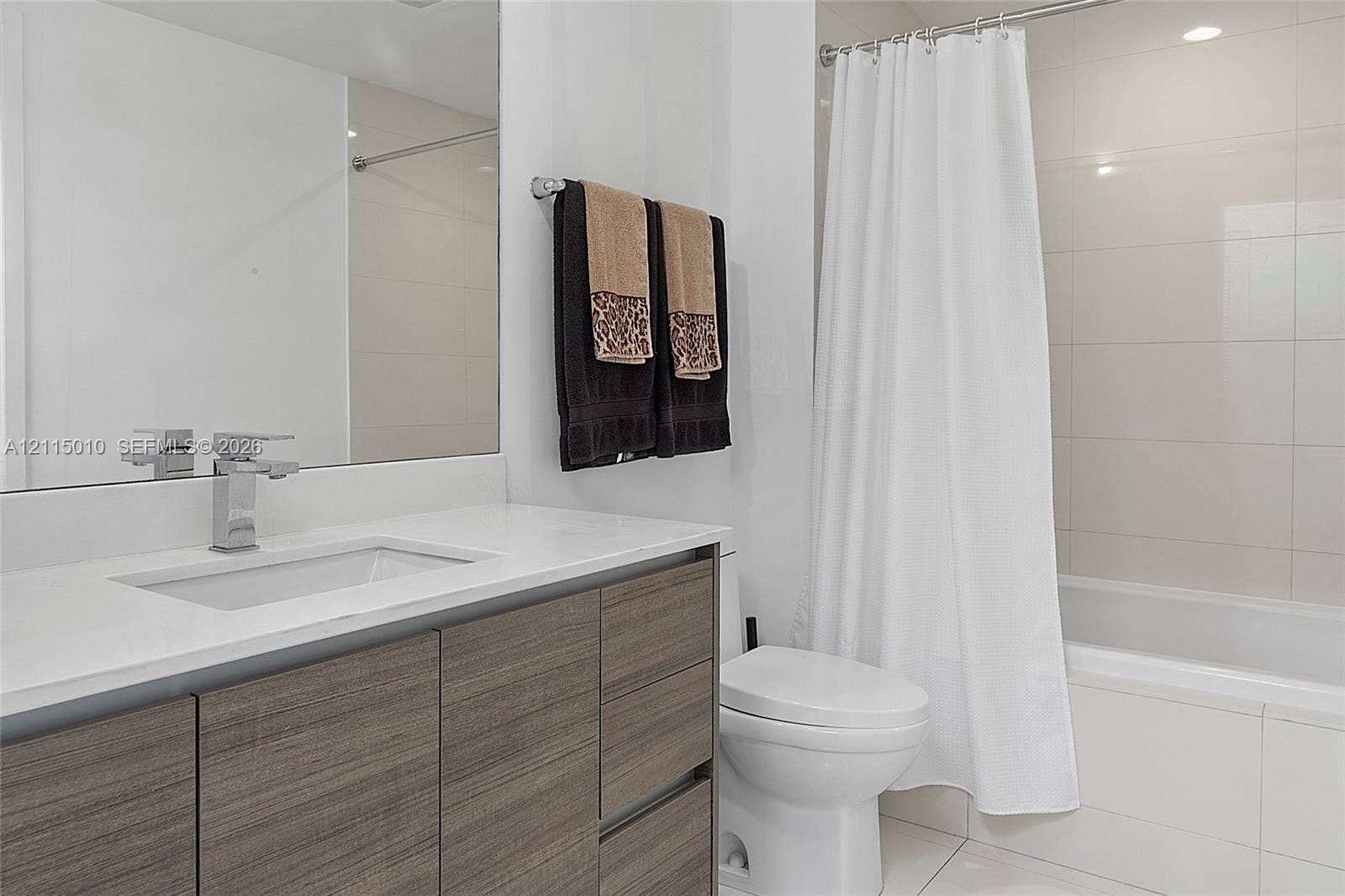 1100 S Miami Avenue, #2407, Miami, FL 33130 Bathroom featuring a flat-panel wood-finish vanity, rectangular undermount sink, stone-surface countertop, chrome single-handle faucet, and full-height tiled shower surround