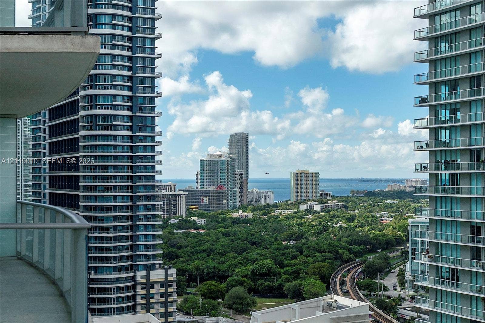 1100 S Miami Avenue, #2407, Miami, FL 33130 Private balcony featuring concrete flooring and a glass-paneled railing overlooking an urban skyline, lush forest canopy, and coastal water