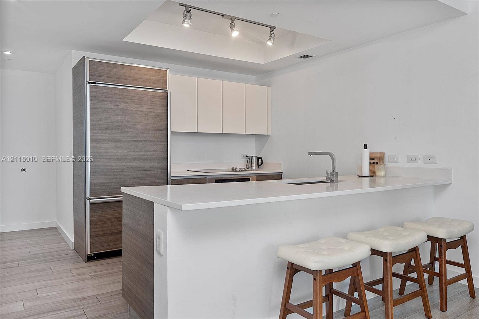 1100 S Miami Avenue, #2407, Miami, FL 33130 Kitchen featuring a stone-surface island with an integrated sink, custom cabinetry with wood-finish paneling, a paneled refrigerator, recessed ceiling lighting, and wood-finish flooring
