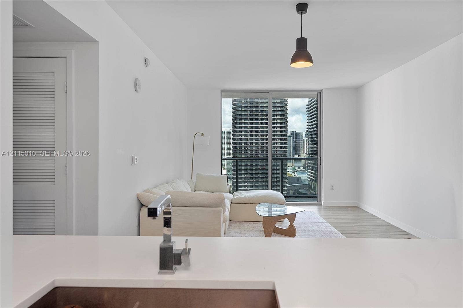 1100 S Miami Avenue, #2407, Miami, FL 33130 Solid surface countertop with a single-handle chrome faucet, floor-to-ceiling glass sliding doors, wood-finish flooring, and a single black industrial-style pendant light