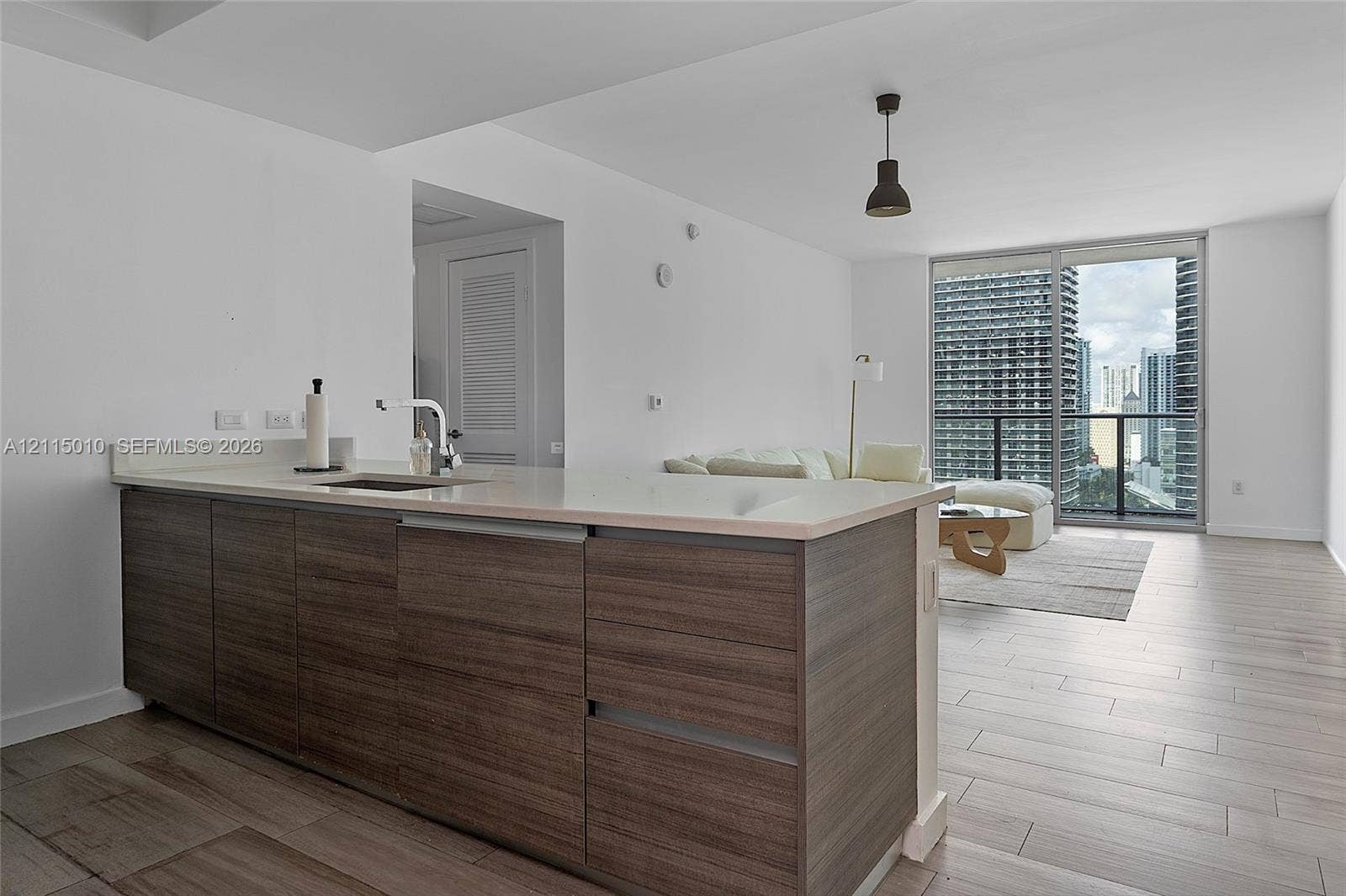 1100 S Miami Avenue, #2407, Miami, FL 33130 Kitchen island featuring wood-finish cabinetry, solid-surface countertop, and an undermount sink, complemented by light-toned tile flooring and expansive sliding glass doors