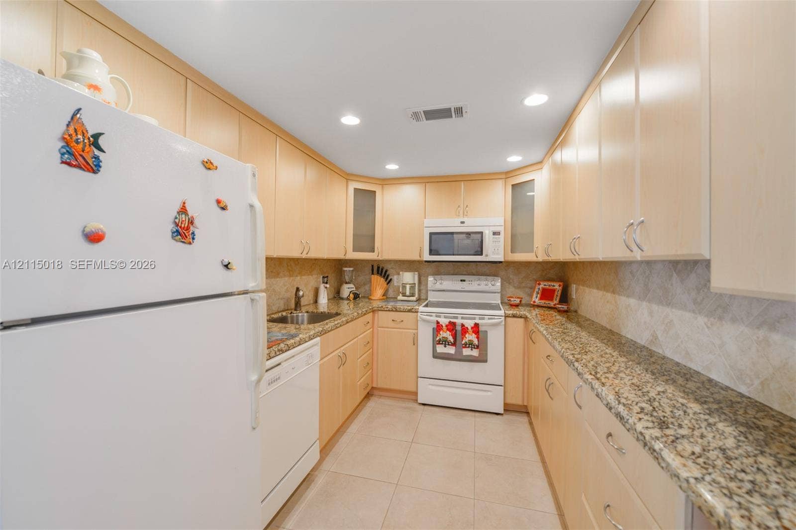 1950 S Ocean Drive, #20N, Hallandale Beach, FL 33009 Galley-style kitchen featuring light wood cabinetry, stone-patterned countertops, a stone tile backsplash, recessed lighting, and large-format tile flooring