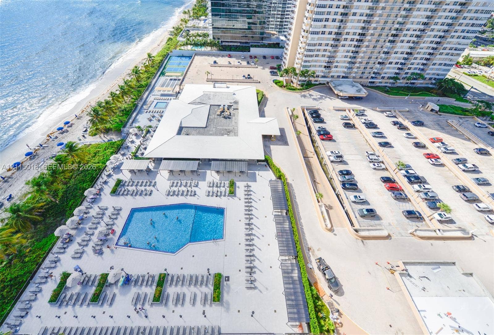 1950 S Ocean Drive, #20N, Hallandale Beach, FL 33009 Aerial perspective of coastal property grounds featuring a swimming pool, paved sundeck, dedicated surface parking, and tennis courts