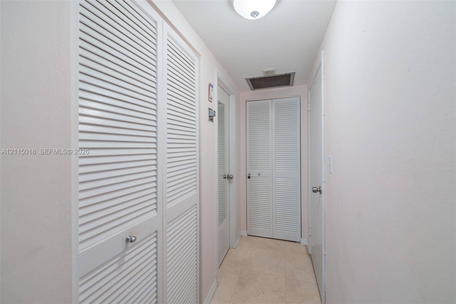 1950 S Ocean Drive, #20N, Hallandale Beach, FL 33009 Hallway featuring neutral tile flooring, multiple louvered-style bi-fold closet doors, and a flush-mount ceiling light fixture