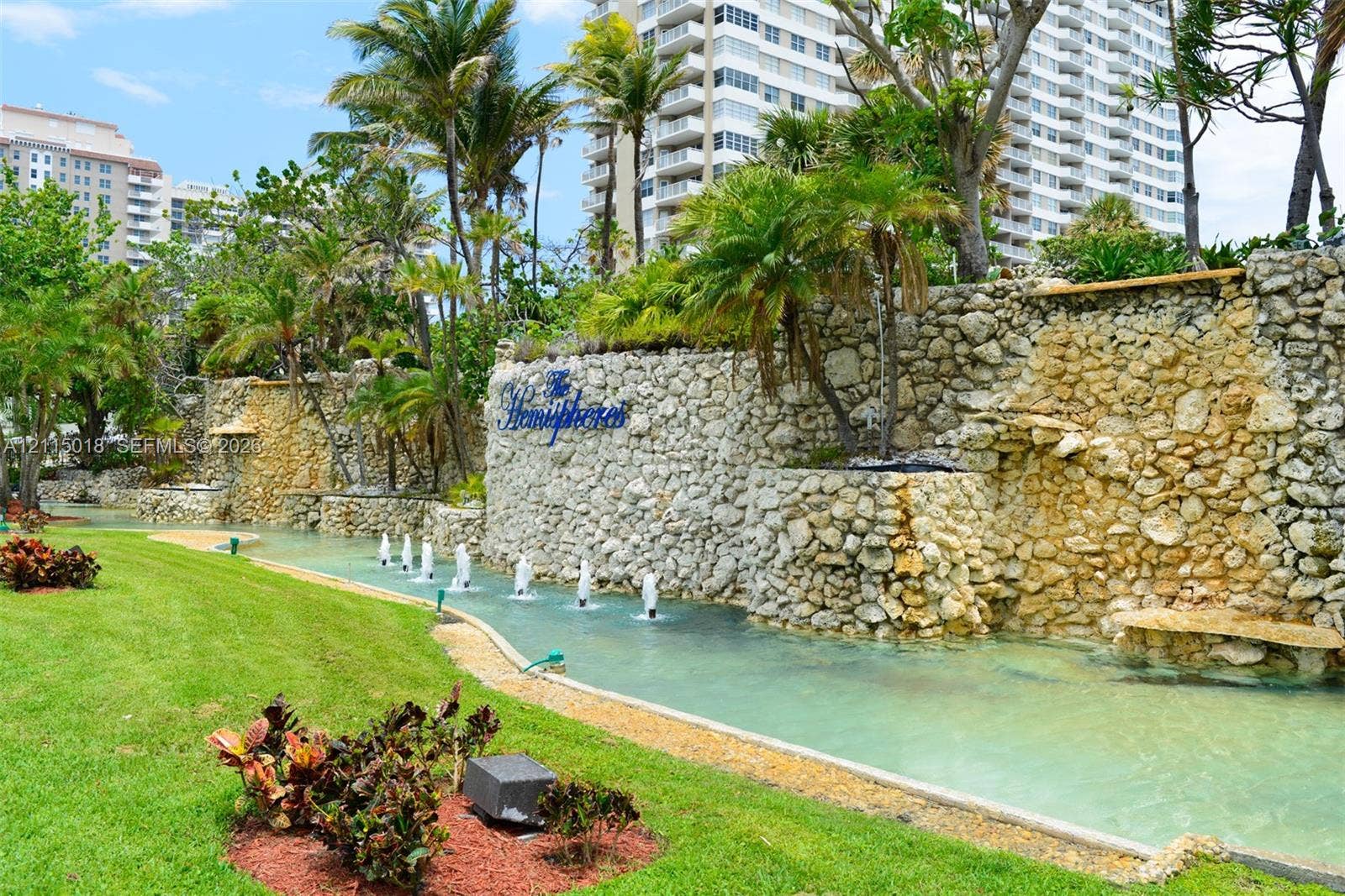 1950 S Ocean Drive, #20N, Hallandale Beach, FL 33009 Landscaped grounds featuring a tiered stone retaining wall, water feature with integrated fountains, manicured lawn, and mature palm trees