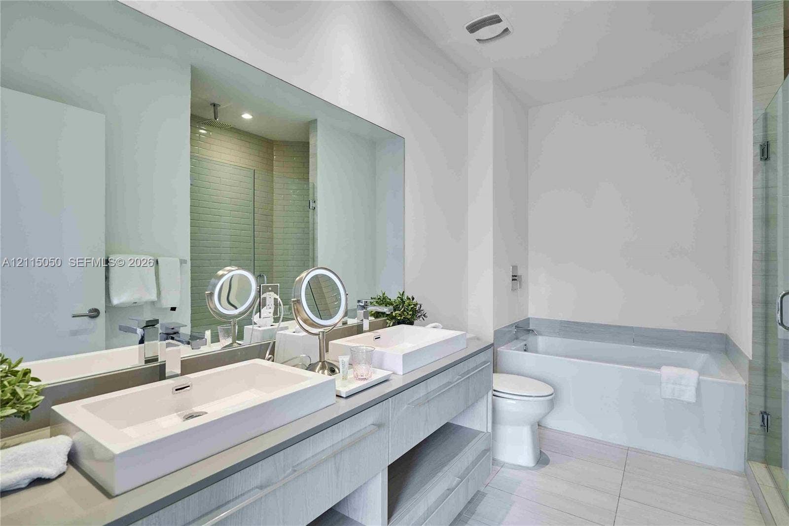 Bathroom featuring a dual-sink floating vanity with rectangular vessel sinks, expansive wall-to-wall mirror, built-in soaking tub, and tiled flooring