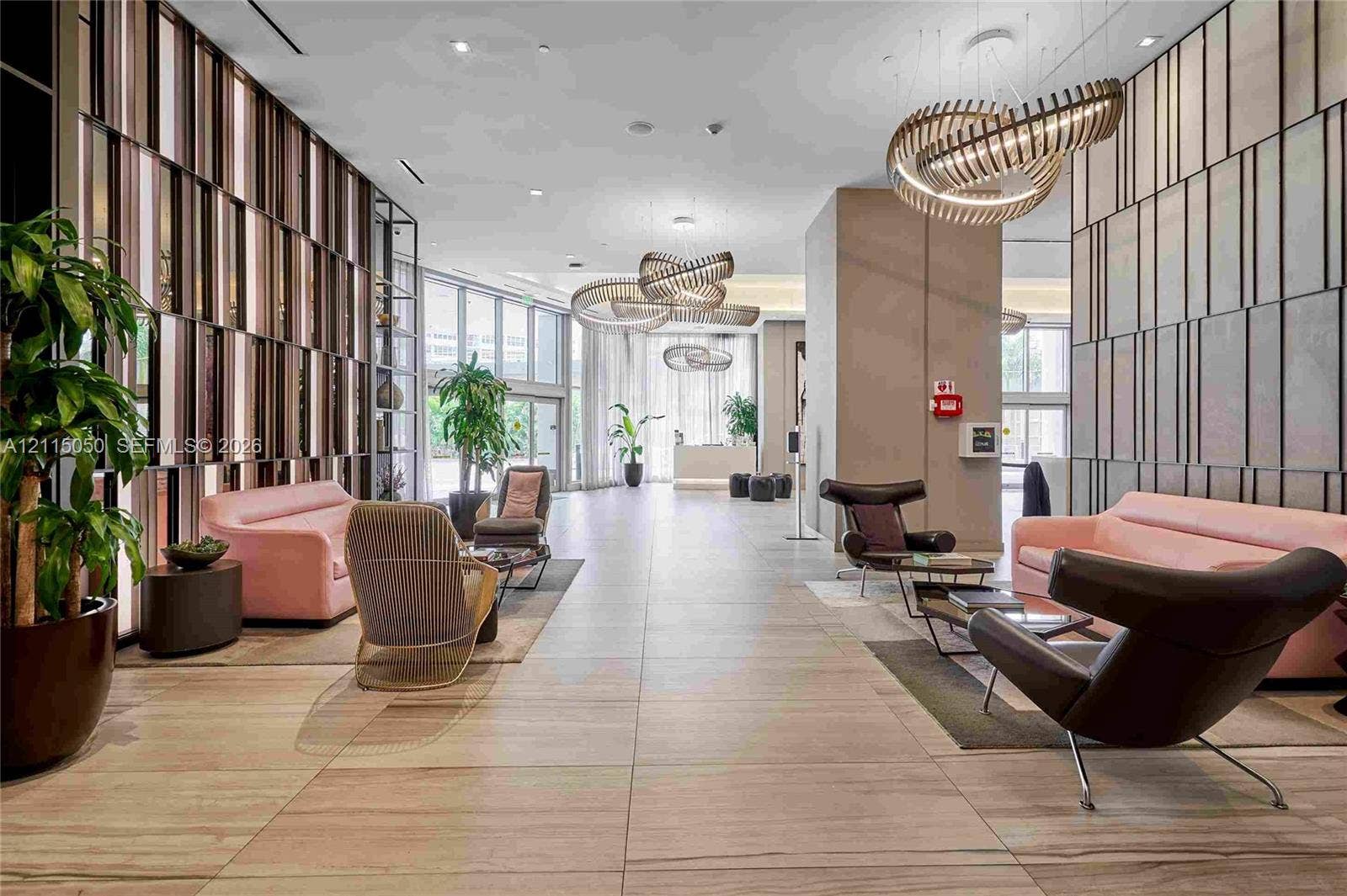 Grand lobby featuring large-format tile flooring, sculptural pendant lighting, floor-to-ceiling glass windows, and textured wall paneling