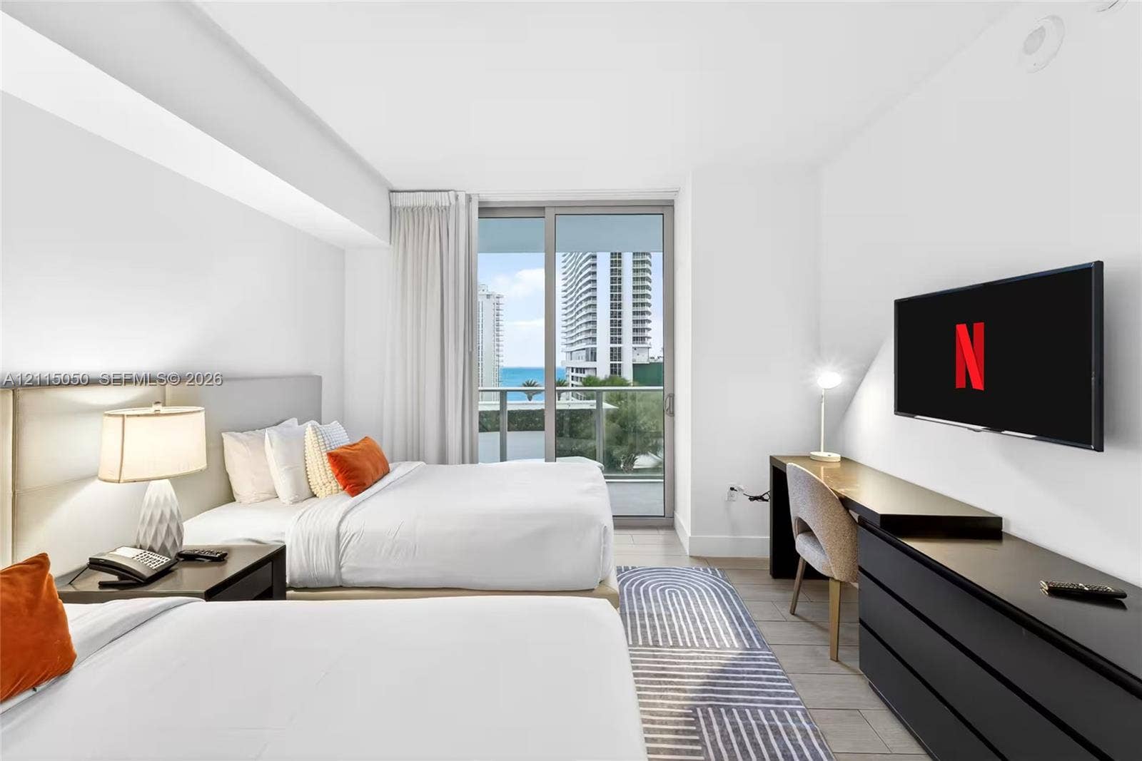 Floor-to-ceiling sliding glass door, private balcony, ocean horizon backdrop, wood-finish flooring, and crisp neutral color palette