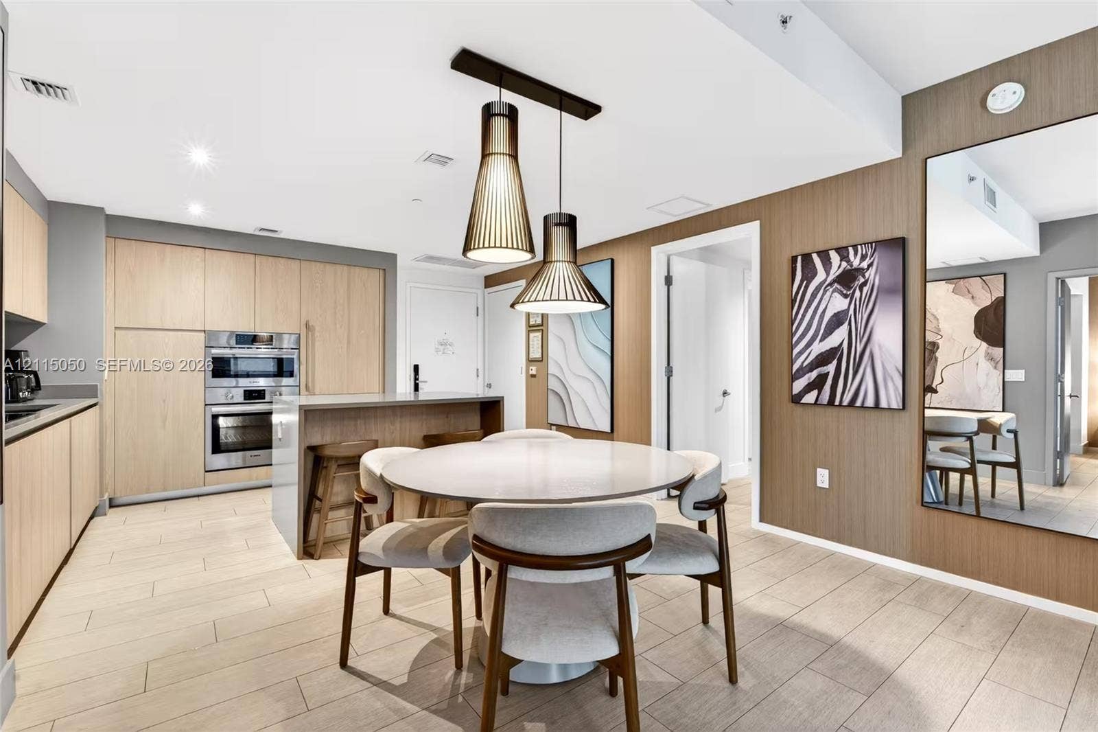 Kitchen featuring flat-panel wood-finish cabinetry, built-in stainless steel double wall ovens, a central island, modern pendant lighting, and wood-finish flooring