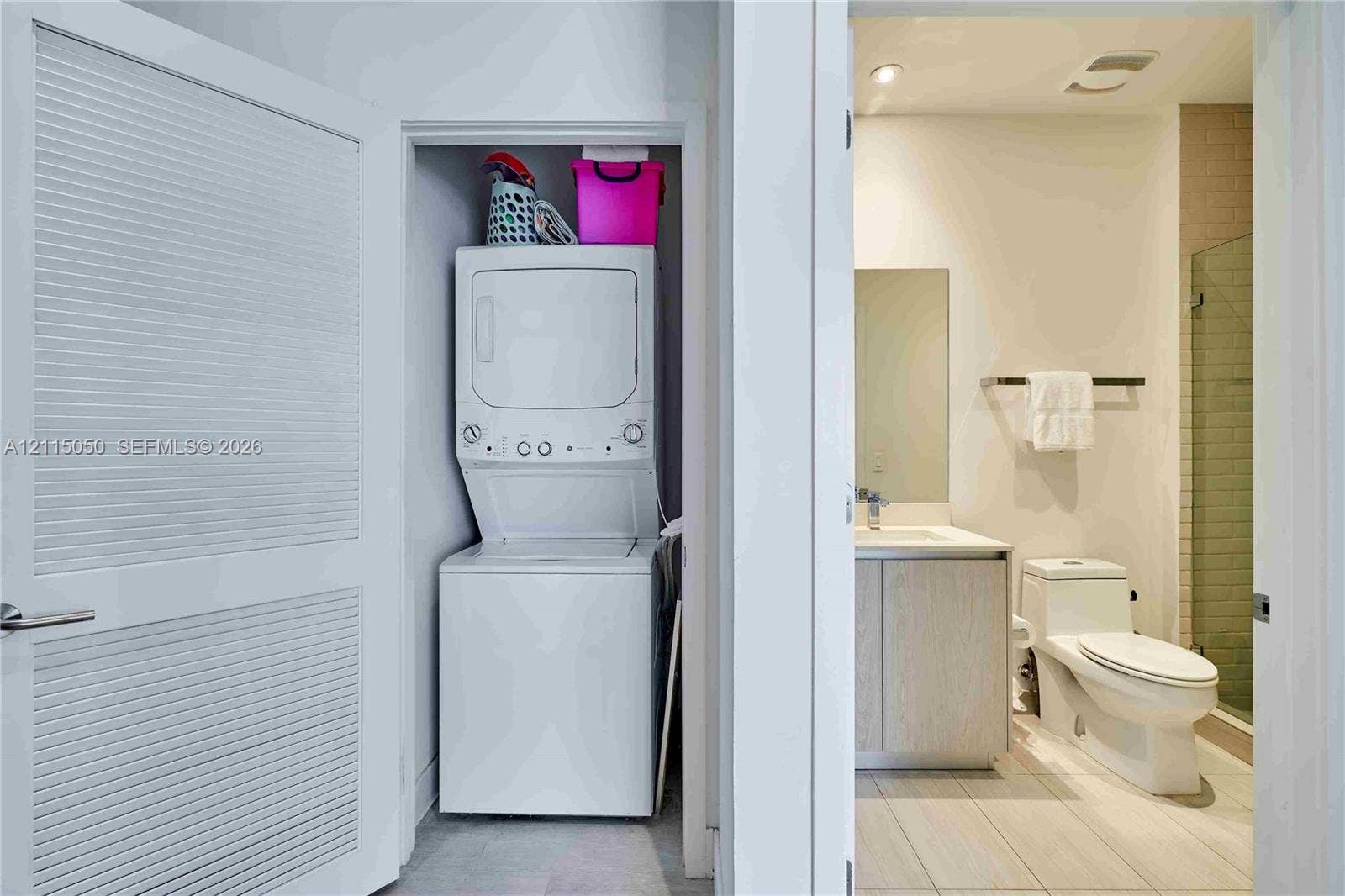 Laundry closet featuring a stacked washer and dryer, paired with a bathroom containing a vanity, a toilet, and a glass-enclosed shower with tiled walls