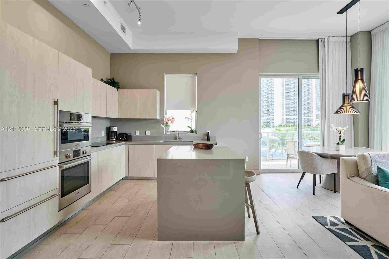 Kitchen featuring light wood-finish cabinetry, a central island with a solid surface countertop, stainless steel double wall ovens, wood-finish flooring, and dual pendant lighting