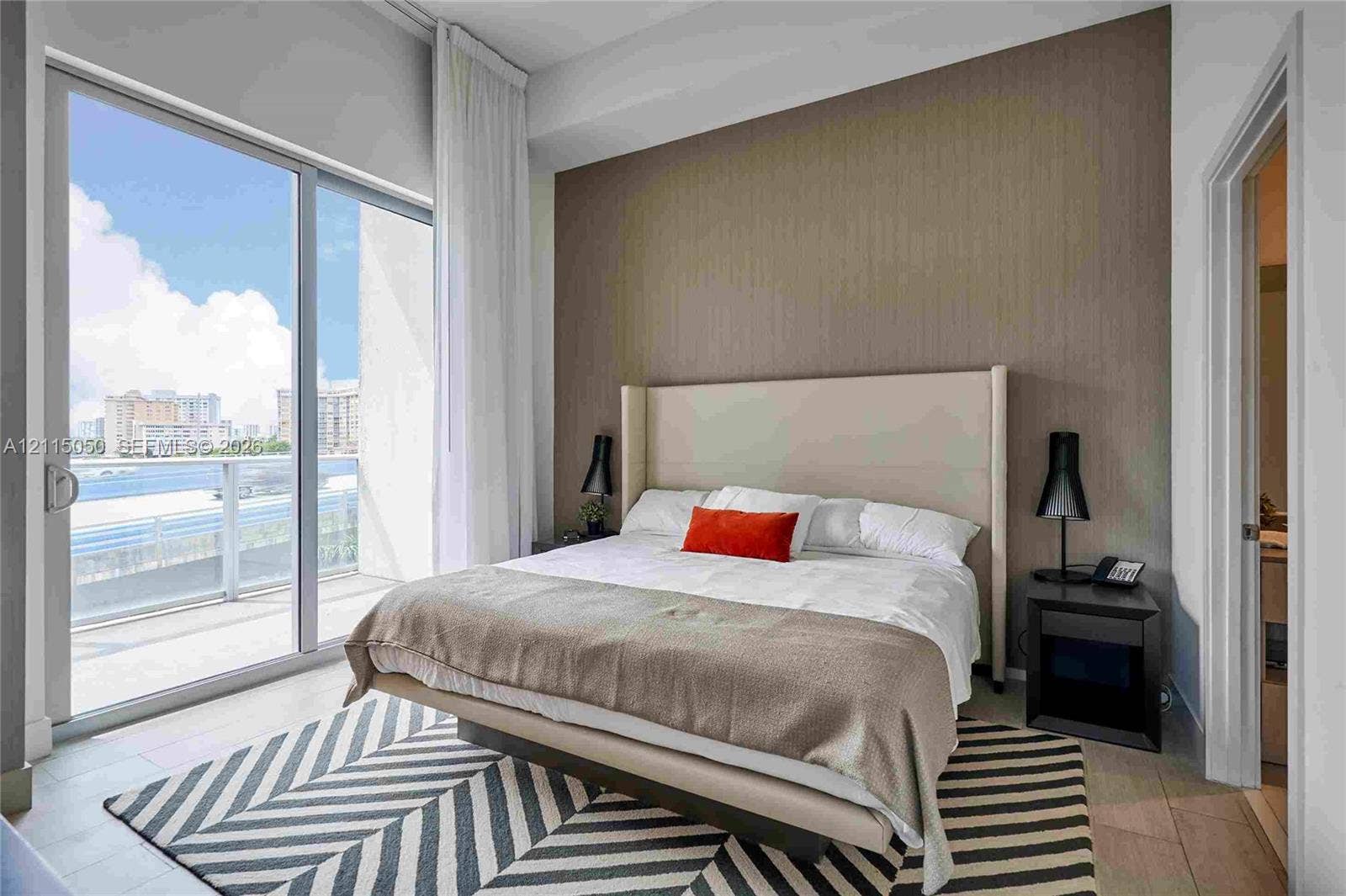Floor-to-ceiling sliding glass door, private balcony, neutral-toned accent wall, and light-colored tile flooring