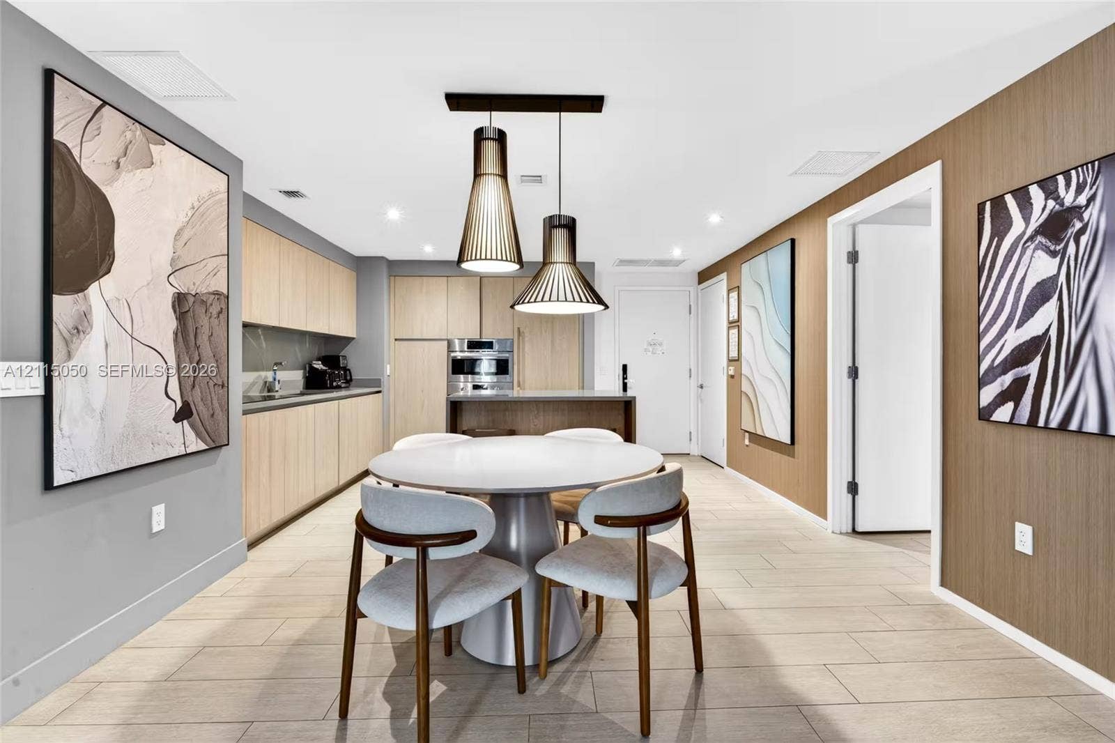 Modern kitchen featuring flat-panel light wood cabinetry, stone-finish countertops, built-in stainless steel appliances, dual geometric pendant lighting, and wood-finish flooring