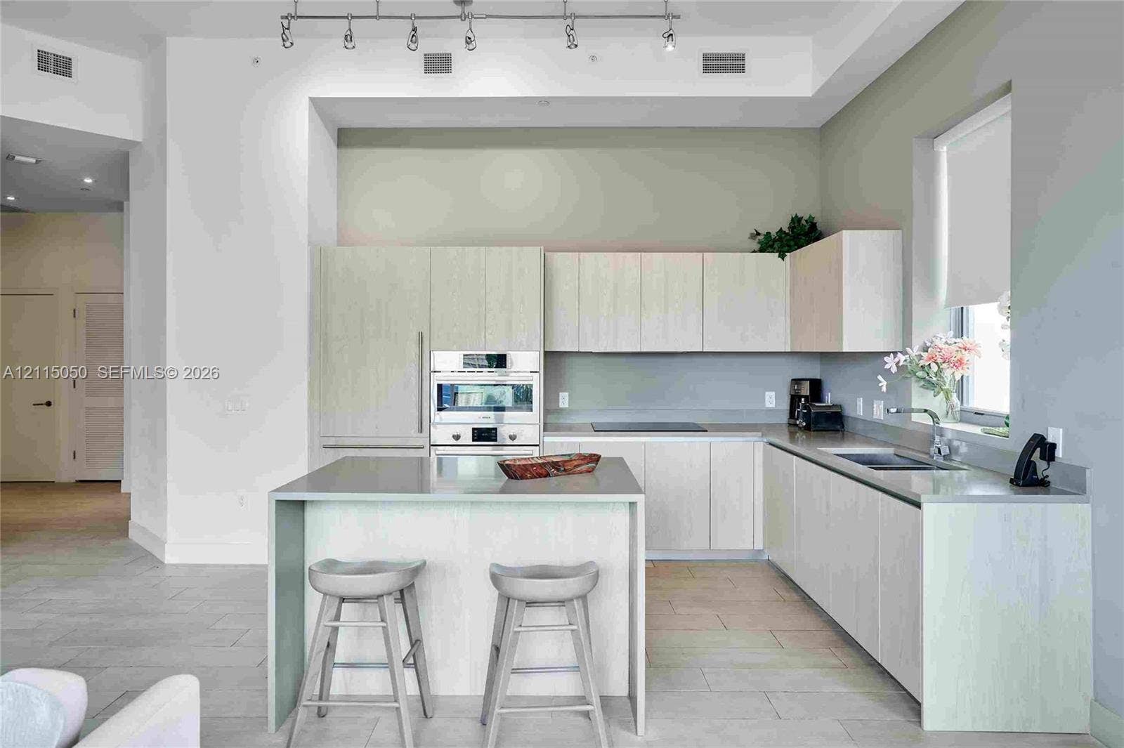 Kitchen featuring light-finish cabinetry, a waterfall-edge island, integrated stainless steel appliances, track lighting, and tile flooring