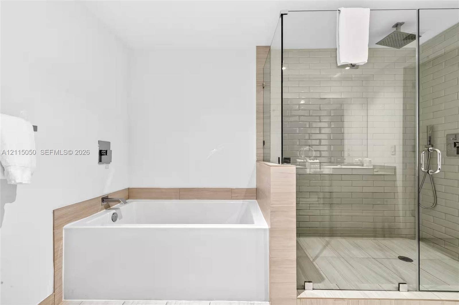 Deep soaking tub with wall-mounted faucet, walk-in glass-enclosed shower, rain-style showerhead, and subway tile wall finishes