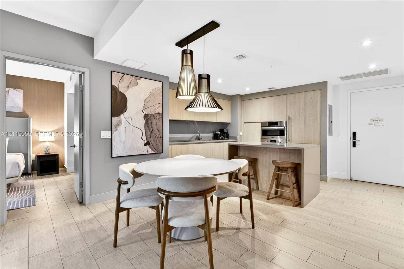 Kitchen featuring wood-finish cabinetry, stone-surface counters, a waterfall-edge kitchen island, integrated stainless steel appliances, and tiered metal pendant lighting over tile flooring