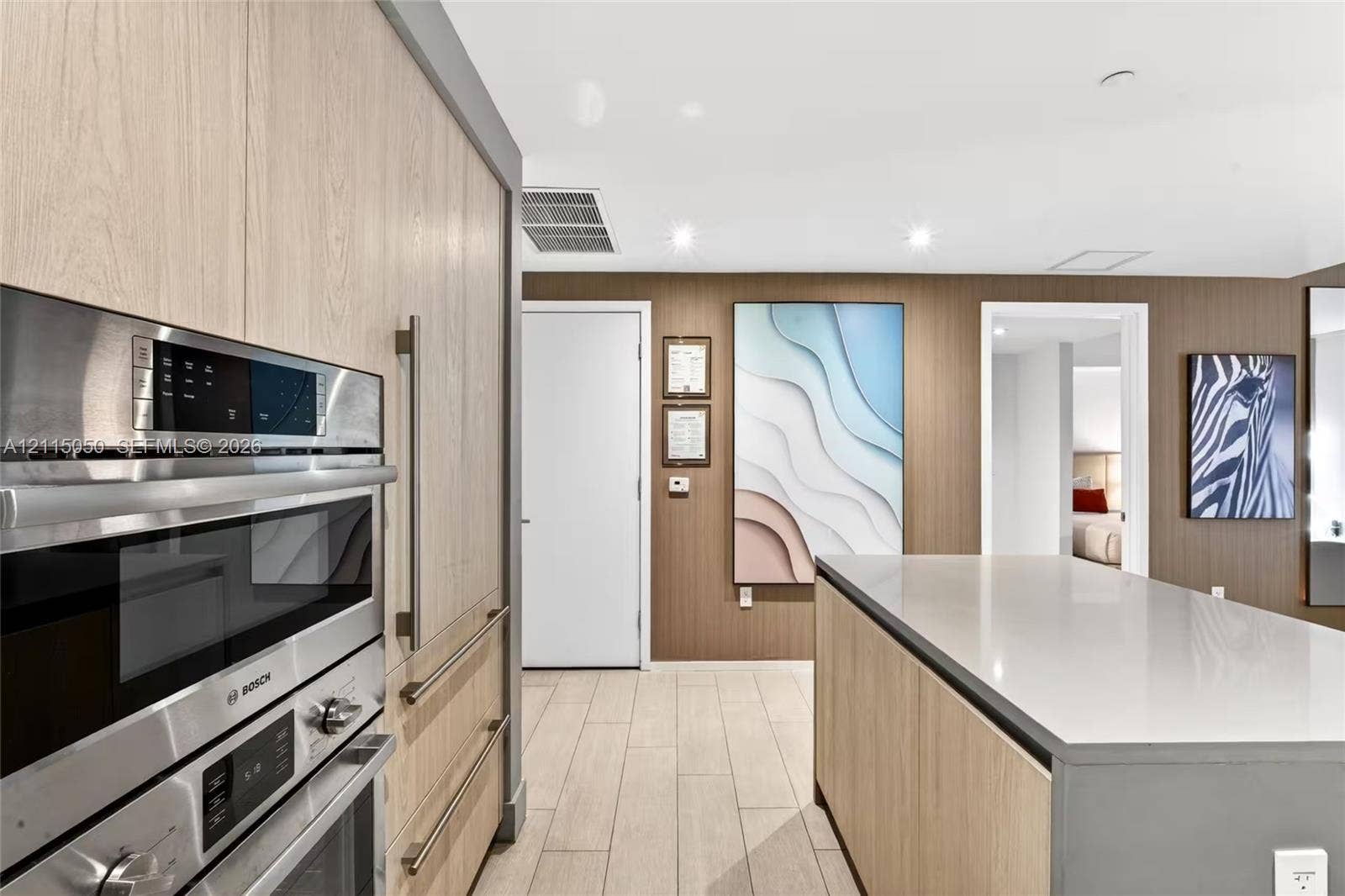 Kitchen featuring light wood-finish cabinetry, a large island with a solid-surface countertop, built-in stainless steel double ovens, and tile flooring