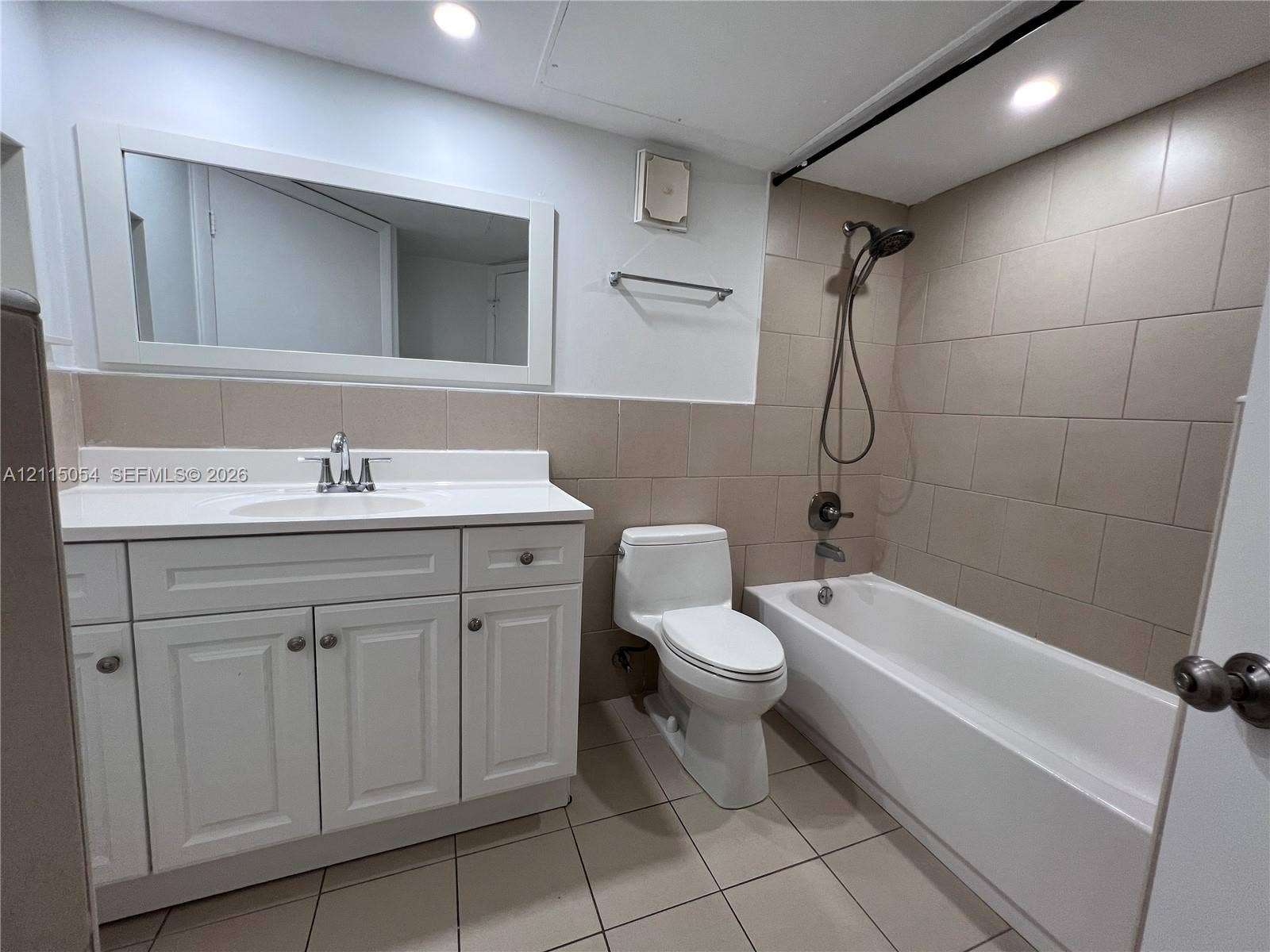 17500 NW 67th Court, #H-19, Hialeah, Hialeah, FL 33015 Bathroom featuring a white vanity with integrated basin, large rectangular wall mirror, tile-surround bathtub with a detachable handheld showerhead, and neutral tile flooring