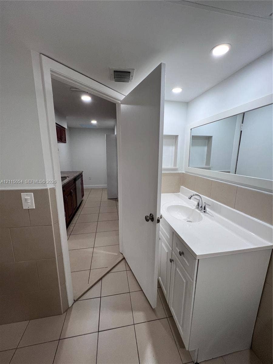 17500 NW 67th Court, #H-19, Hialeah, Hialeah, FL 33015 Bathroom vanity with a white cabinet, integrated sink, chrome faucet, and rectangular mirror, featuring tile flooring and tile wall accents