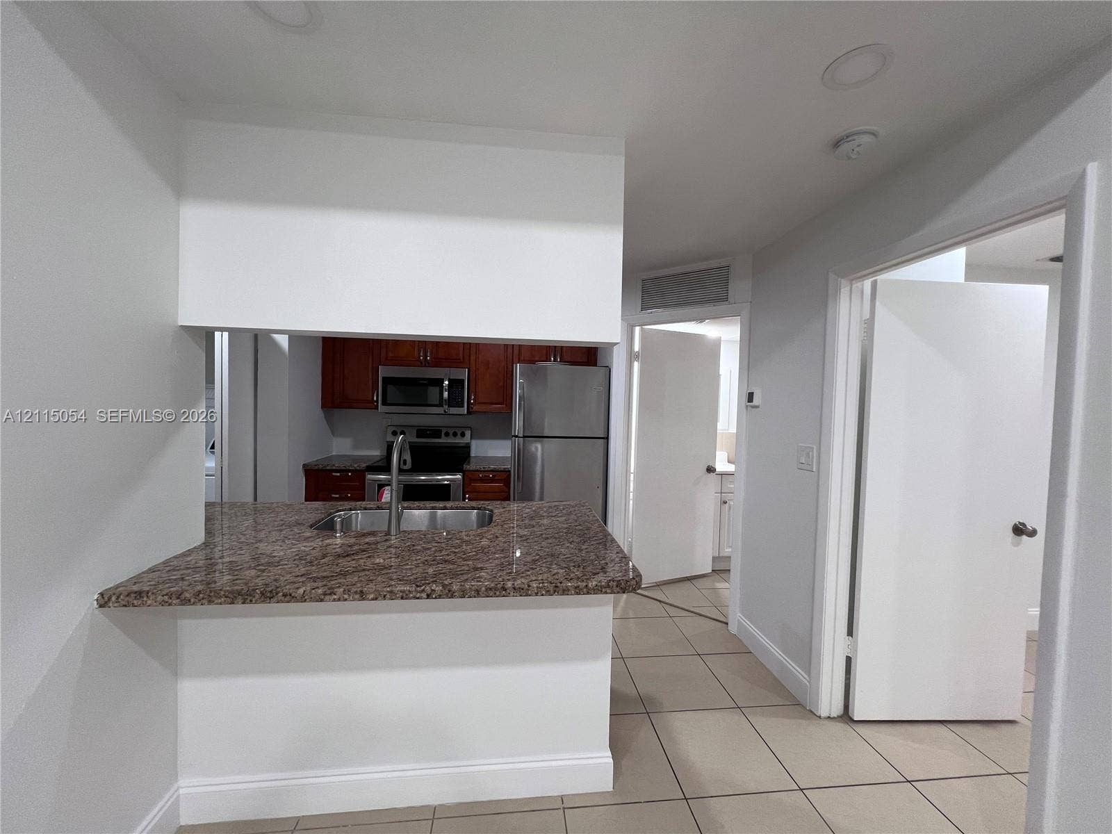 17500 NW 67th Court, #H-19, Hialeah, Hialeah, FL 33015 Pass-through kitchen counter with a stone-finish surface, stainless steel double-basin sink, wood-finish cabinetry, stainless steel appliances, and ceramic tile flooring