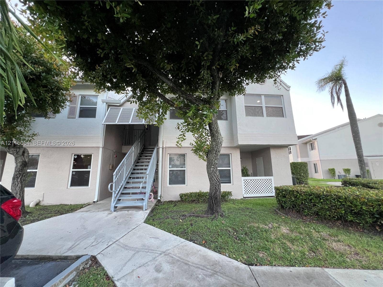 17500 NW 67th Court, #H-19, Hialeah, Hialeah, FL 33015 Two-story stucco exterior featuring a metal staircase, covered landing, decorative lattice screen, and mature landscape