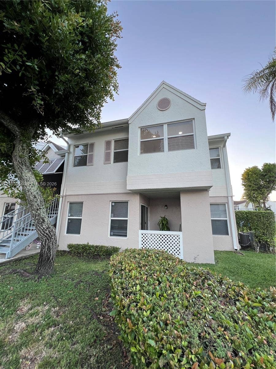 17500 NW 67th Court, #H-19, Hialeah, Hialeah, FL 33015 Two-story exterior featuring a light-toned stucco facade, dual-pane windows, a covered ground-level patio with lattice railing, and metal staircase access