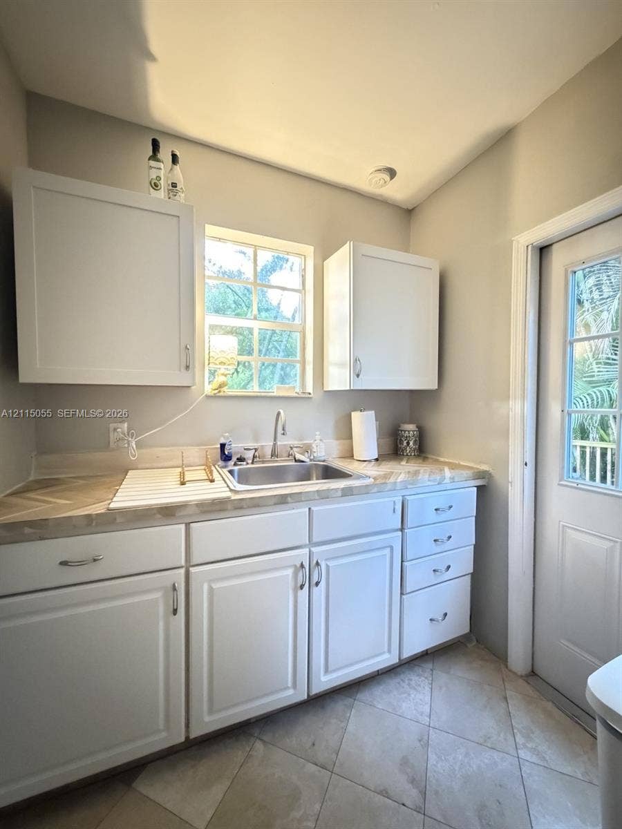 11728 NE 6th Avenue, #2, Biscayne Park, Biscayne Park, FL 33161 White cabinetry featuring shaker-style doors, herringbone-patterned laminate countertops, undermount stainless steel sink, tile flooring, and a glass-paneled exterior door