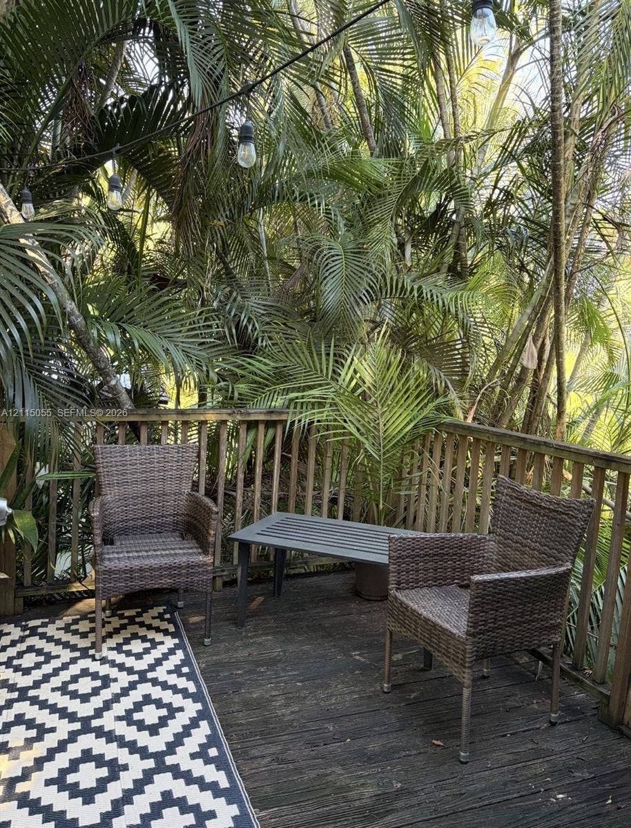 11728 NE 6th Avenue, #2, Biscayne Park, Biscayne Park, FL 33161 Outdoor deck featuring wood planking, vertical wood balustrades, and overhead string lighting, surrounded by mature palm trees