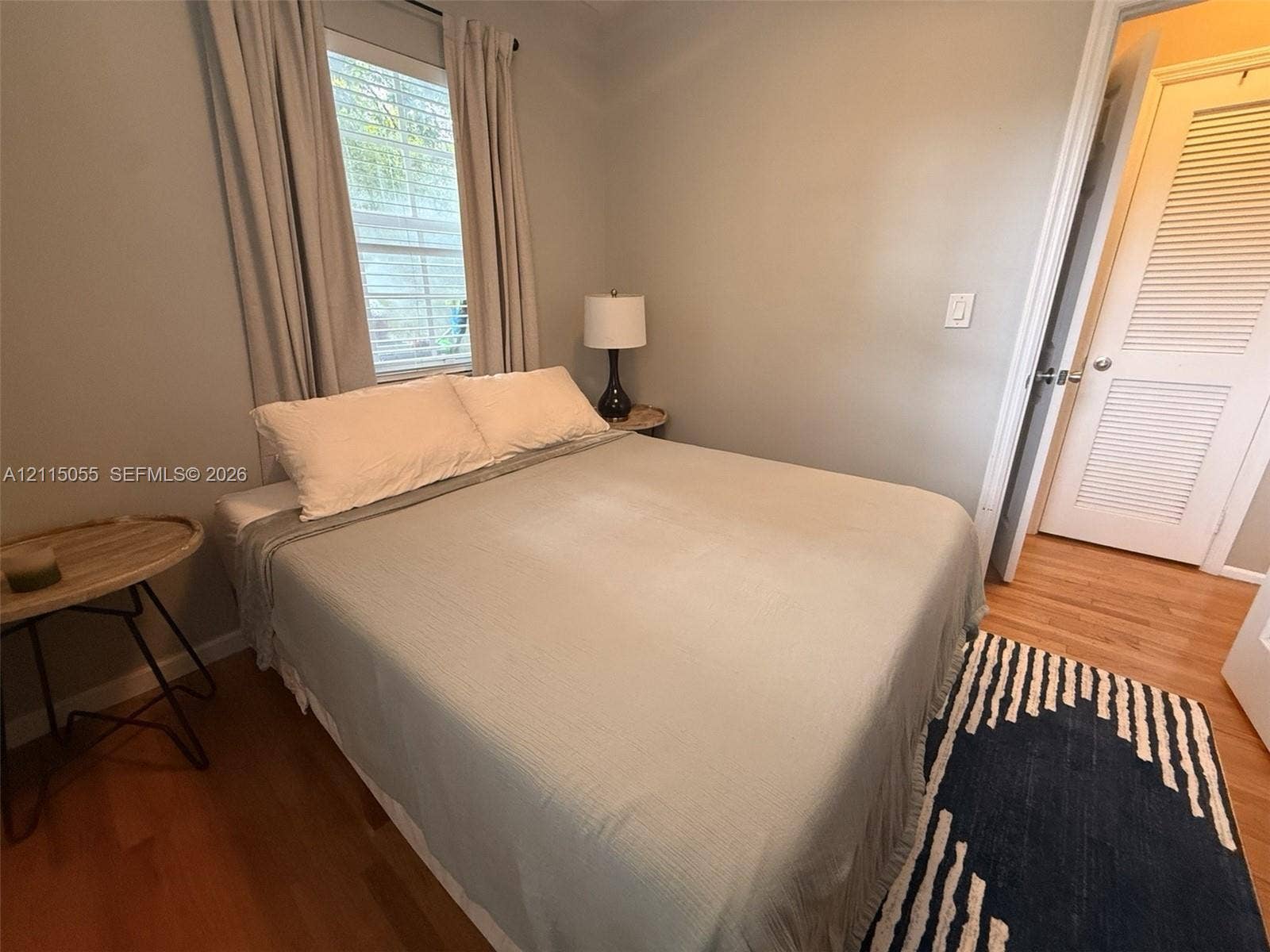 11728 NE 6th Avenue, #2, Biscayne Park, Biscayne Park, FL 33161 Neutral-toned interior room featuring wood-finish flooring, a single window with horizontal blinds, and a louvered-panel door